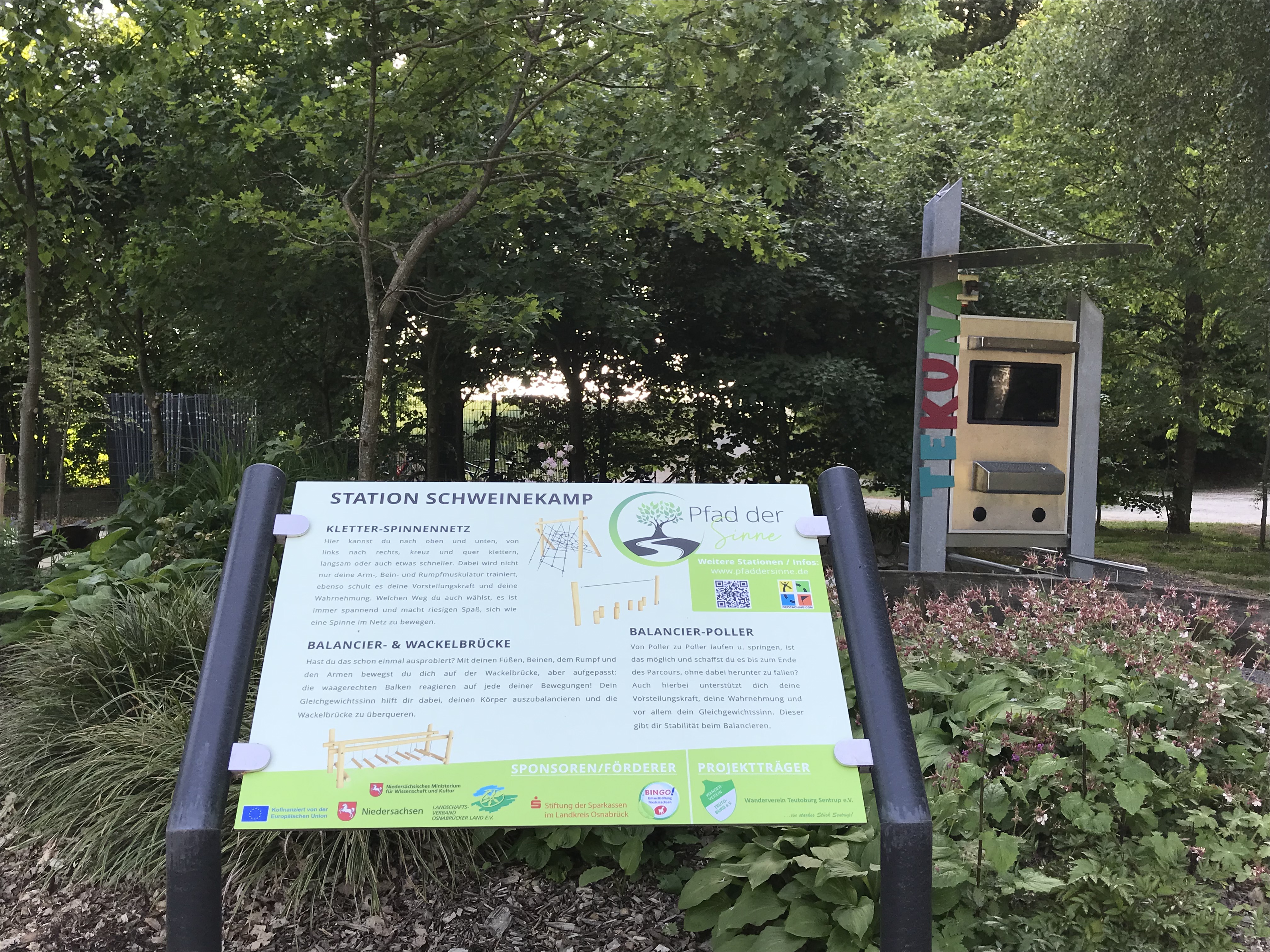 Infotafel an der Station Schweinekamp, dahinter Spielgerät und Bäume