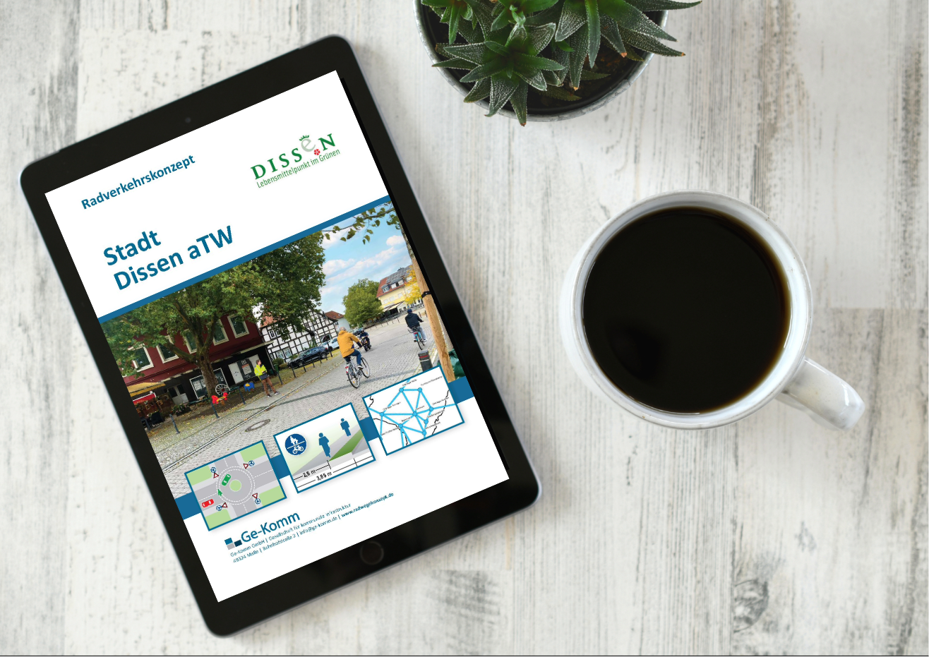 Eine Tischplatte mit Kaffee und Grünpflanze sowie einem Tablet, auf dem das Titelbild des Radverkehrskonzept Dissen aTW zu sehen ist