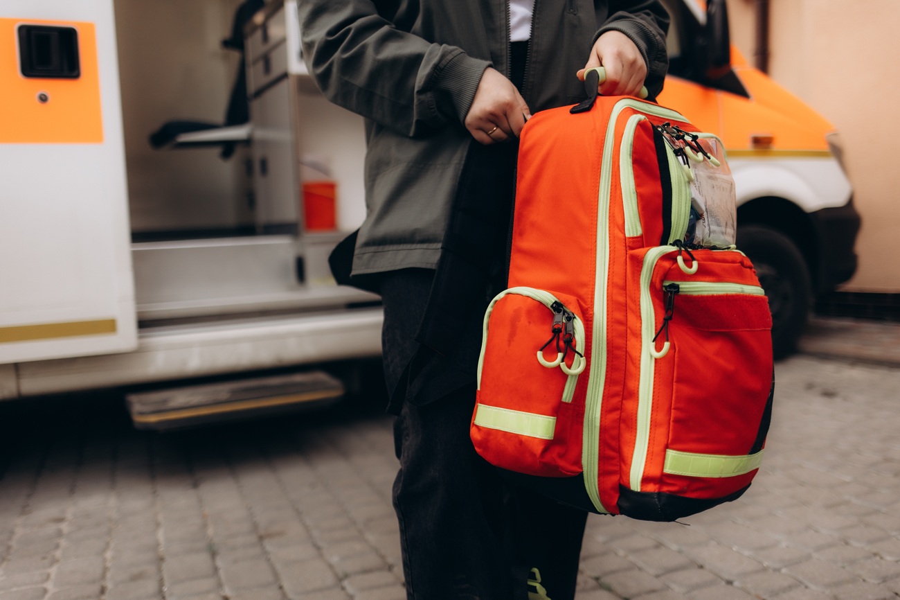 Eine Person trägt einen Notfallrucksack, dahinter Rettungswagen